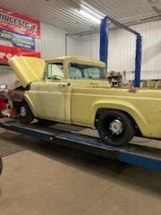 Vintage yellow pickup truck on a lift inside an auto repair shop with its hood open.